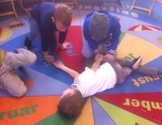 Kinder üben gemeinsam Erste-Hilfe-Maßnahmen auf einem Teppich und lernen spielerisch grundlegende Kenntnisse zur Hilfeleistung.