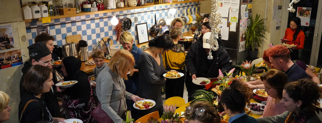 Blick von oben auf ein variantenreiches Buffet, Menschen bestaunen es und nehmen sich Speisen auf ihre Teller. 