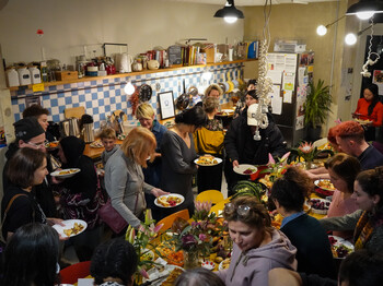 Blick von oben auf ein variantenreiches Buffet, Menschen bestaunen es und nehmen sich Speisen auf ihre Teller. 