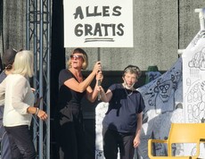 Menschen mit einem Schild "alles gratis" vor einem weiß-schwarzem Papierhaus