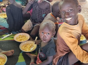 Zwei Kinder im Ernährungszentrum essen und grinsen in die Kamera