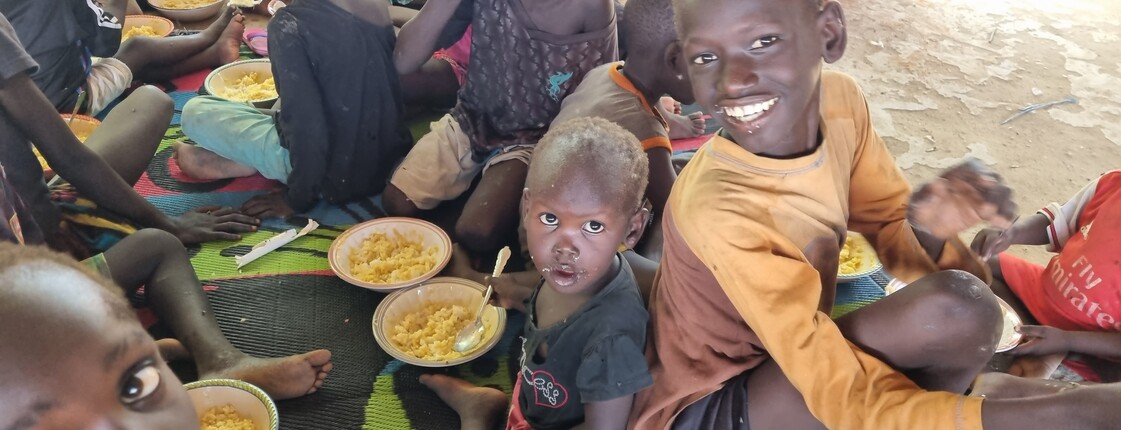 Zwei Kinder im Ernährungszentrum essen und grinsen in die Kamera