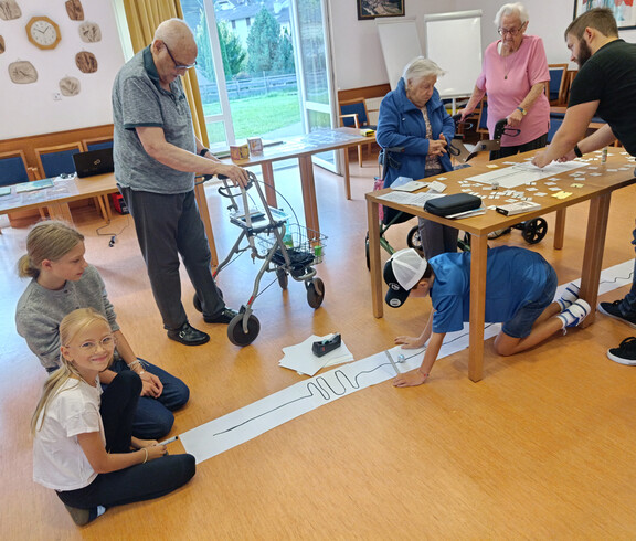 Kinder und Senior*innen programmieren gemeinsam einen Mini-Roboter auf Papierstrecke im Festsaal