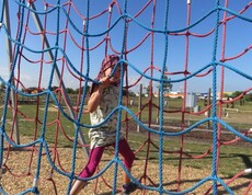 Ein Kind klettert auf einem bunten Kletternetz im Motorikpark und trainiert spielerisch Beweglichkeit sowie Koordination.