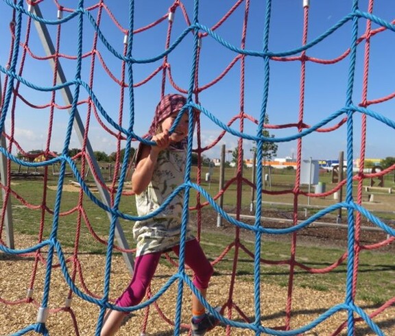 Ein Kind klettert auf einem bunten Kletternetz im Motorikpark und trainiert spielerisch Beweglichkeit sowie Koordination.