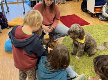 Kinder sitzen gemeinsam mit einem Therapiehund im Klassenraum. Die Begegnung fördert Aufmerksamkeit, soziale Kompetenzen und Vertrauen.