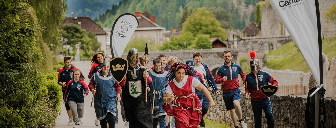 Gruppe läuft verkleidet und sportlich beim Caritas-Charity-Lauf mit Fahnen in bergiger Landschaft