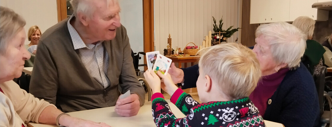 Kind zeigt Spielkarten einer Gruppe von Senior*innen am Tisch