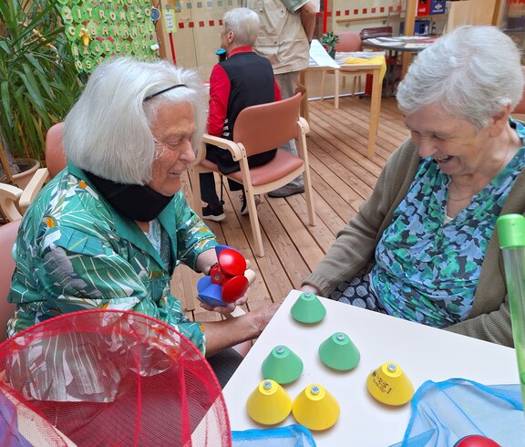 Zwei Bewohnerinnen eines Pflegewohnhauses sitzen an einem Tisch und beschäftigen sich im Rahmen einer Aktion zum Tag der Demenz mit bunten Spiel- und Bewegungsmaterialien.