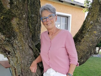 Eine Frau steht im Freien an einen Baum gelehnt und lächelt.