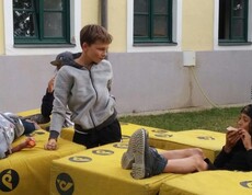 Kinder sitzen und stehen auf weichen Bauelementen im Freien, machen eine Pause und verbringen gemeinsam Zeit bei einer Gruppenaktivität.