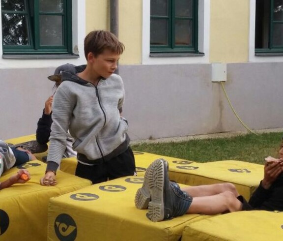 Kinder sitzen und stehen auf weichen Bauelementen im Freien, machen eine Pause und verbringen gemeinsam Zeit bei einer Gruppenaktivität.