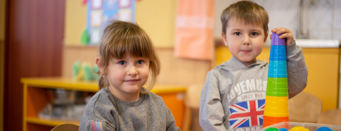 Zwei Kinder spielen im Kinder- und Familienzentrum Charkiw, Ukraine. Ein Junge baut einen Turm aus bunten Bechern, während ein Mädchen lächelt.