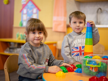Zwei Kinder spielen im Kinder- und Familienzentrum Charkiw, Ukraine. Ein Junge baut einen Turm aus bunten Bechern, während ein Mädchen lächelt.