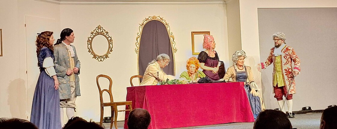Fünf Schauspieler in Kostüm auf der Bühne, zwei sitzen an einem Tisch