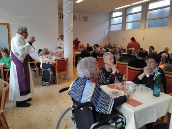 Pfarrer spricht vor Bewohner*innen im festlich dekorierten Speisesaal