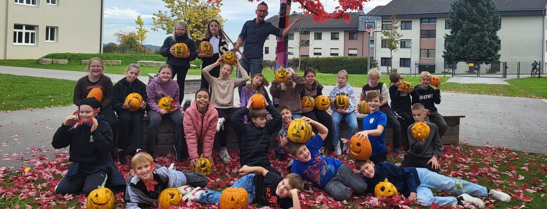 Gruppenbild der Jugendlichen vor einem Baum mit herbstlich roten Blättern und mit den gestalteten Kürbissen. 