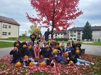 Gruppenbild der Jugendlichen vor einem Baum mit herbstlich roten Blättern und mit den gestalteten Kürbissen. 