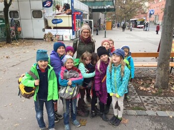 Eine Kindergruppe mit Begleitperson versammelt sich auf einem städtischen Platz und startet gemeinsam zu einem Ausflug im Freien.