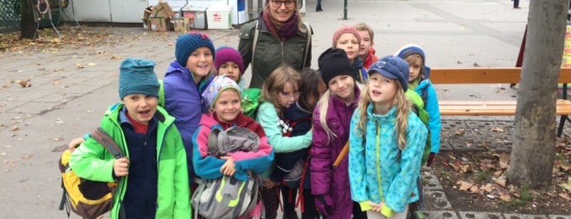 Eine Kindergruppe mit Begleitperson versammelt sich auf einem städtischen Platz und startet gemeinsam zu einem Ausflug im Freien.