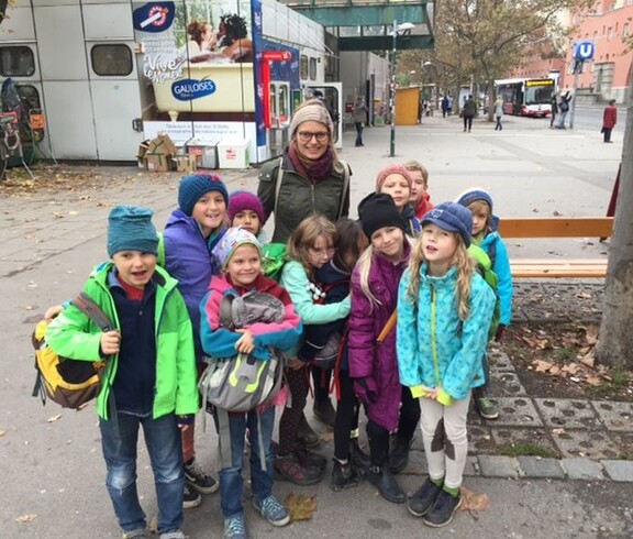 Eine Kindergruppe mit Begleitperson versammelt sich auf einem städtischen Platz und startet gemeinsam zu einem Ausflug im Freien.