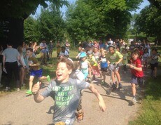 Kinder starten gemeinsam bei einer Laufveranstaltung im Freien und laufen nach dem Startsignal entlang einer Parkstrecke los.