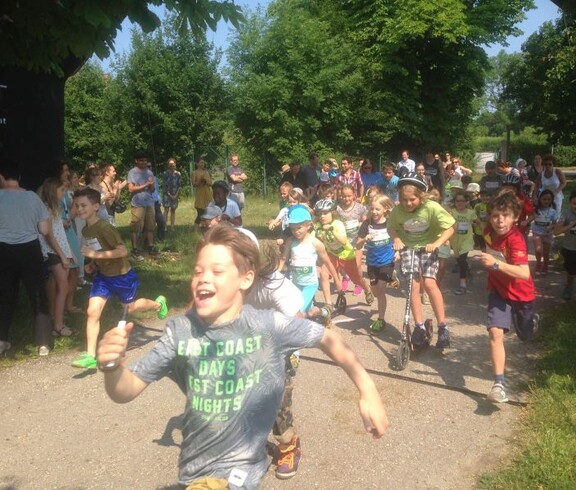 Kinder starten gemeinsam bei einer Laufveranstaltung im Freien und laufen nach dem Startsignal entlang einer Parkstrecke los.