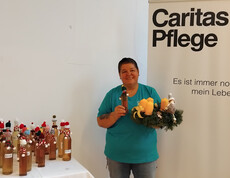 Eine Person steht neben einem Tisch mit dekorierten Flaschen und hält eine Flasche und einen Kranz mit Kerzen.