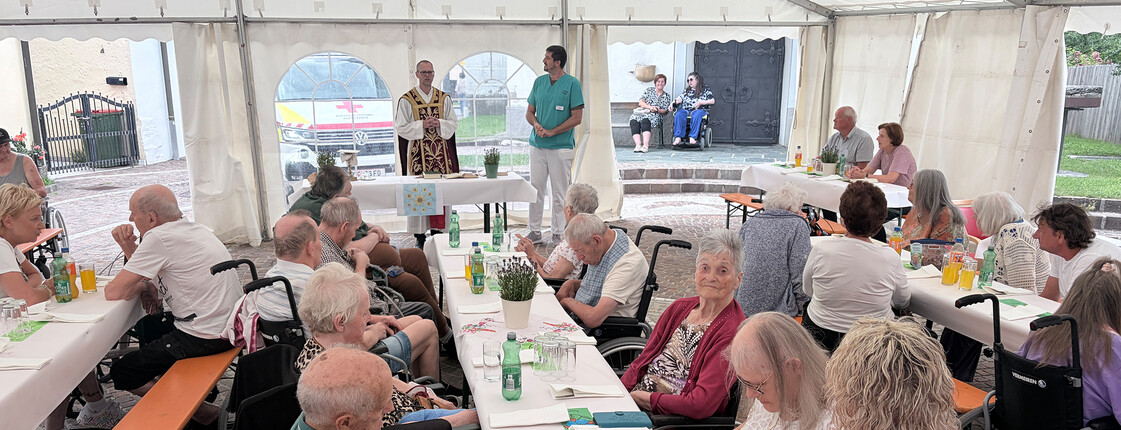 Gäste sitzen im Festzelt, während eine Ansprache vor dem Altar des Sommerfests im Haus Theresia stattfindet.