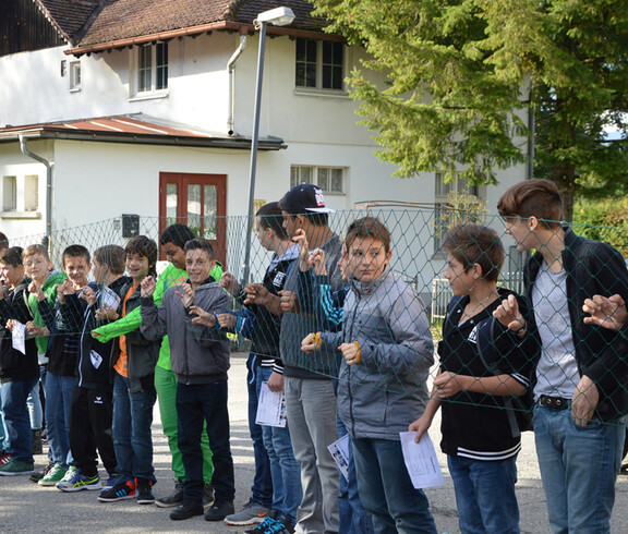 Viele Kinder stehen hinter einem Zaun im Freien.
