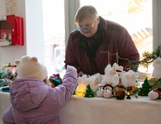 Kleines Mädchen übernimmt auf einem Weihnachtsmarkt ein Produkt von einer Frau