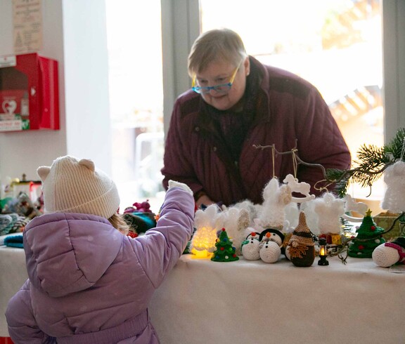 Kleines Mädchen übernimmt auf einem Weihnachtsmarkt ein Produkt von einer Frau