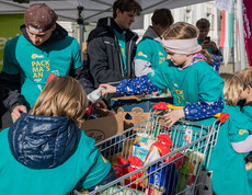 Kinder legen gespendete Lebensmittel in Kartons, unterstützt von Helfern der youngCaritas.