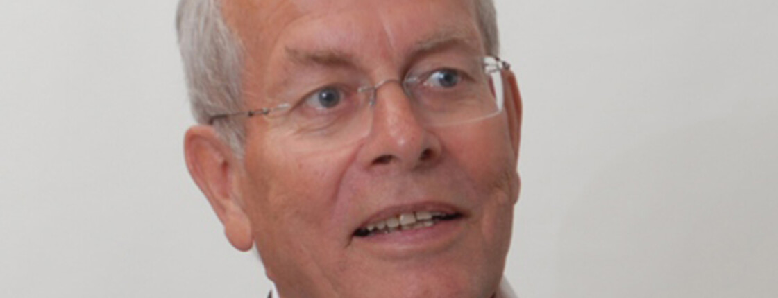 Ein älterer Herr trägt eine Brille und ein Sakko. 
