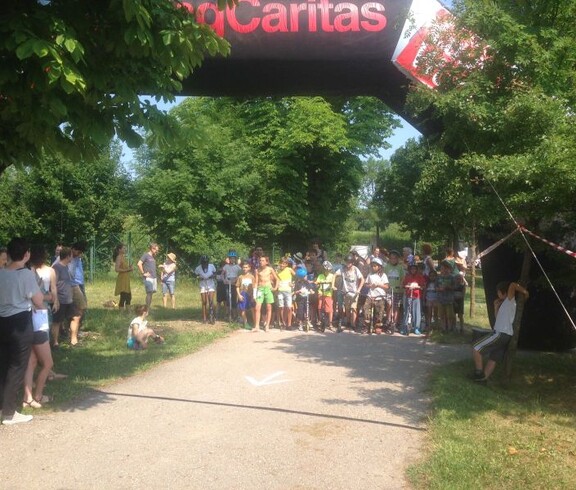 Kinder versammeln sich mit Rollern unter einem Startbogen im Park und bereiten sich gemeinsam auf den Beginn einer Sportveranstaltung vor.