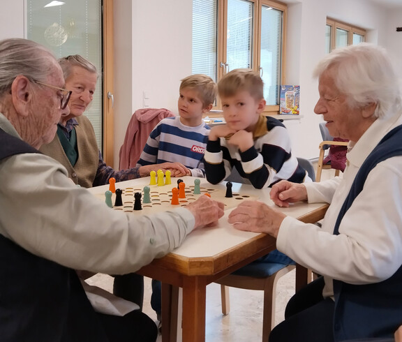 Kinder und Senior*innen spielen zusammen ein Brettspiel am Tisch