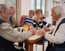 Kinder und Senior*innen spielen zusammen ein Brettspiel am Tisch