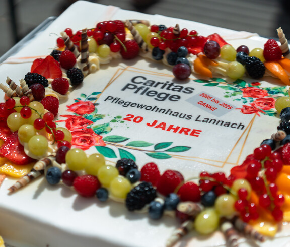 Eine rechteckige Torte mit bunten Früchten und Dekorationen. In der Mitte steht der Text: „Caritas Pflege – Pflegewohnhaus Lannach – 20 Jahre – 2005 bis 2025 – Danke“.