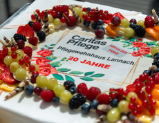 Eine rechteckige Torte mit bunten Früchten und Dekorationen. In der Mitte steht der Text: „Caritas Pflege – Pflegewohnhaus Lannach – 20 Jahre – 2005 bis 2025 – Danke“.