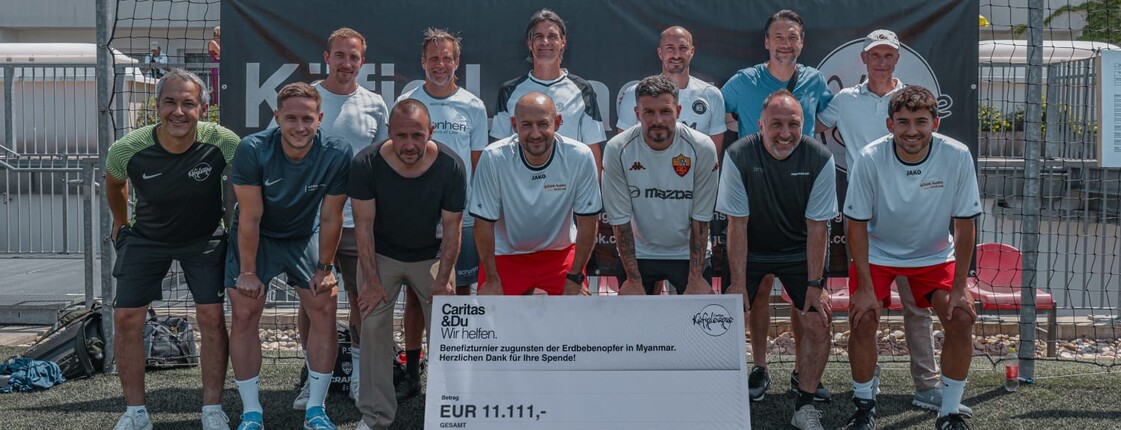 13 Männer stehen in Fußballuniform vor einem Fußballtor. Vor ihnen ist ein großer Scheck über 11.111 Euro zu sehen, der den Erdbebenopfer von Myanmar zugute kommen wird.