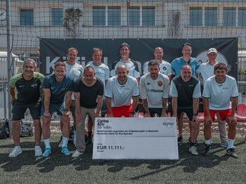 13 Männer stehen in Fußballuniform vor einem Fußballtor. Vor ihnen ist ein großer Scheck über 11.111 Euro zu sehen, der den Erdbebenopfer von Myanmar zugute kommen wird.
