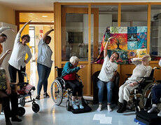 Pflegekraft leitet Senior*innen im Rollstuhl zu einer achtsamen Bewegungseinheit im Aufenthaltsraum an.