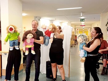 Vier schwarz gekleidete Puppenspieler stehen vor den Bewohner*innen des Caritas Pflegewohnhauses Lannach und führen eine Puppenshow auf. Die Szene zeigt eine lebendige Unterhaltung im Pflegealltag.