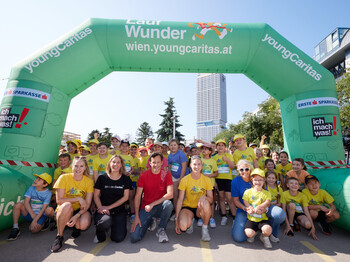 Viele Erwachsene und Kinder in Lauf-Gewand winken lächelnd unter der Startlinie der Laufstrecke eines Benifiz-Laufes.