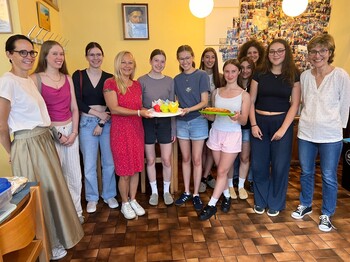 Zwei Lehrerinnen stehen mit Schüler*innen in der Katharina-Stube und präsentieren mit der Dienststellenleiterin einen kuchen.