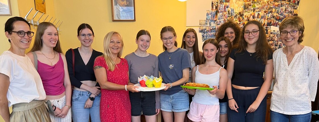 Zwei Lehrerinnen stehen mit Schüler*innen in der Katharina-Stube und präsentieren mit der Dienststellenleiterin einen kuchen.