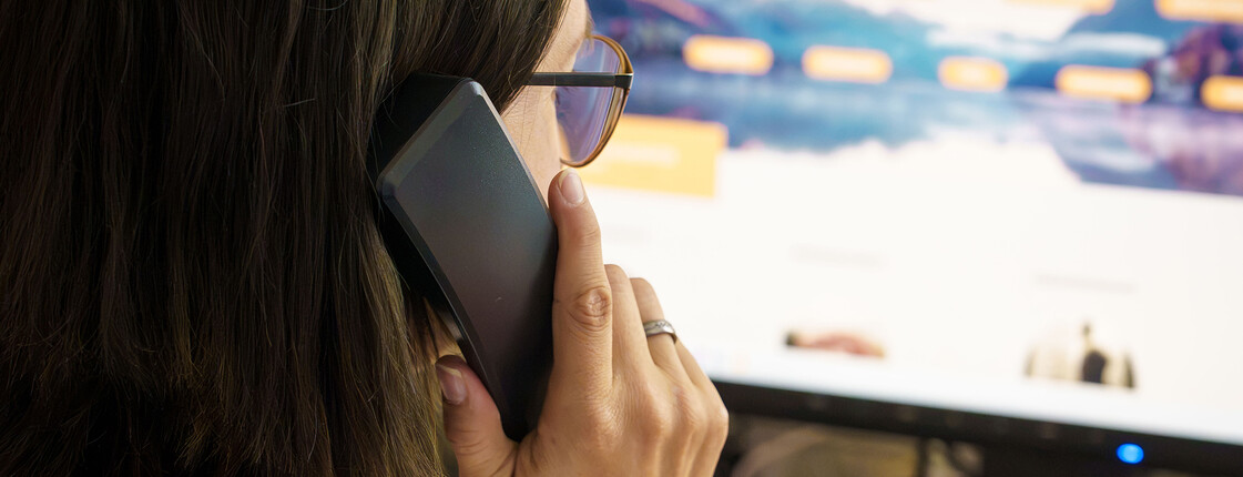 Eine Braunhaarige mit Brille hält einen Telefonhörer in der Hand und sieht dabei auf den Bildschirm, auf dem man die Website der Telefonseelsorge Österreich leicht verschwommen sieht.