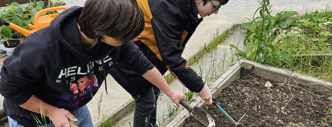 Zwei Kinder lockern die Erde in einem Hochbeet mit Gartenwerkzeugen auf. Das gemeinsame Gärtnern fördert Naturerfahrung und Verantwortung.