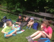 Kinder sitzen während einer Projektwoche auf einer Wiese am Waldrand, machen eine Pause und verbringen gemeinsam Zeit im Freien.