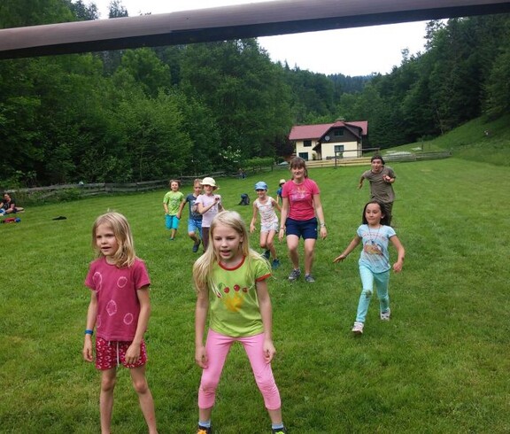Kinder nehmen auf einer großen Wiese an einem Bewegungsspiel teil und verbringen während der Projektwoche gemeinsam aktive Zeit im Freien.